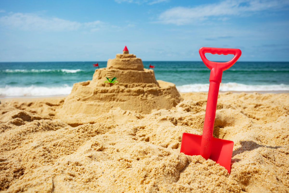 Sand castle on the beach with a red shovel resting beside it, showcasing a sunny day at the seaside.