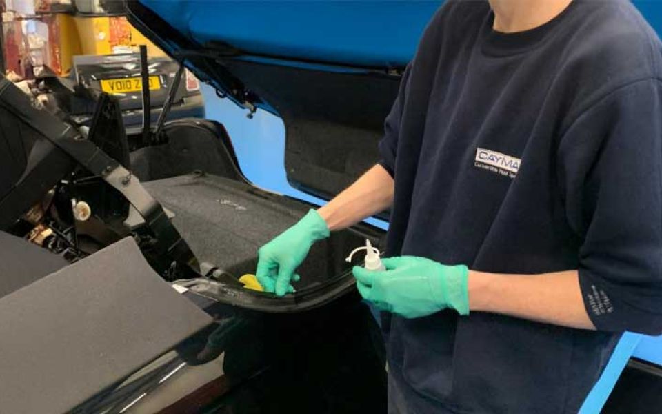 A man wearing a blue shirt and gloves is repairing a car in a garage.