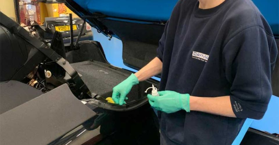 A man wearing a blue shirt and gloves is repairing a car in a garage.
