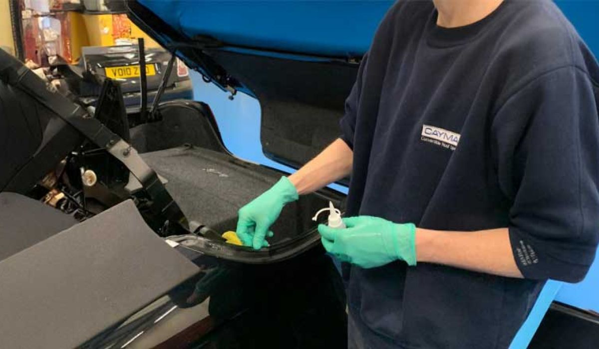 A man wearing a blue shirt and gloves is repairing a car in a garage.