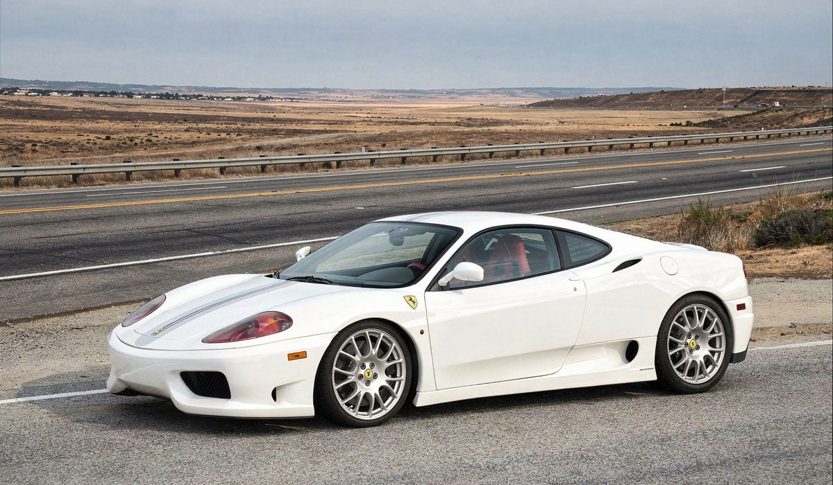 A white Ferrari sports car speeds along a winding road under a clear blue sky.