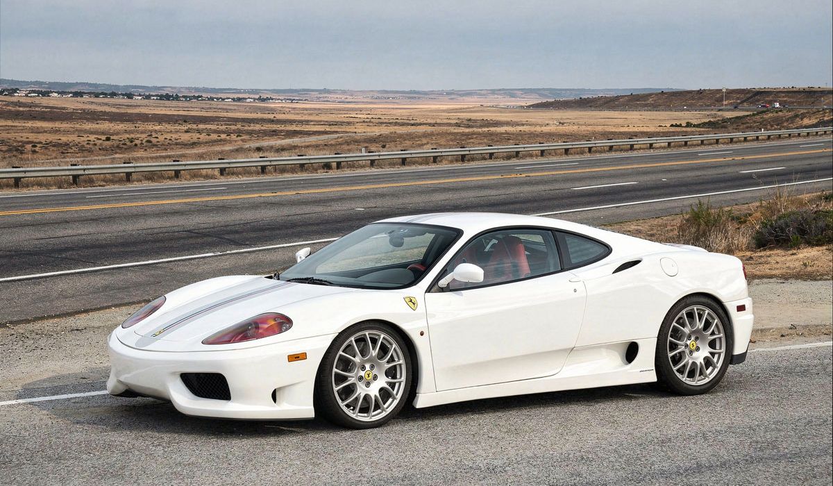 A white Ferrari sports car speeds along a winding road under a clear blue sky.