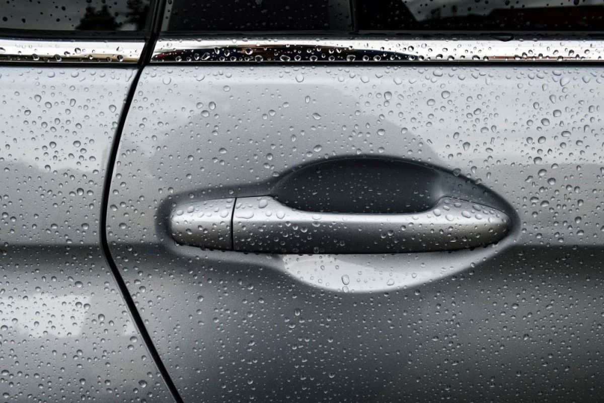 Car door handle covered in rain droplets on a grey vehicle, highlighting exterior detailing and water ingress protection.