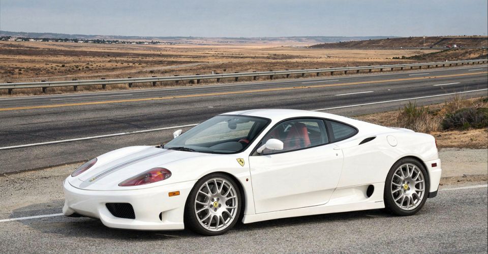 A white Ferrari sports car speeds along a winding road under a clear blue sky.