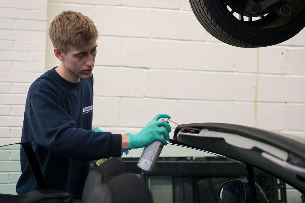 Technician applying maintenance spray to a convertible soft top roof during professional annual roof maintenance service.