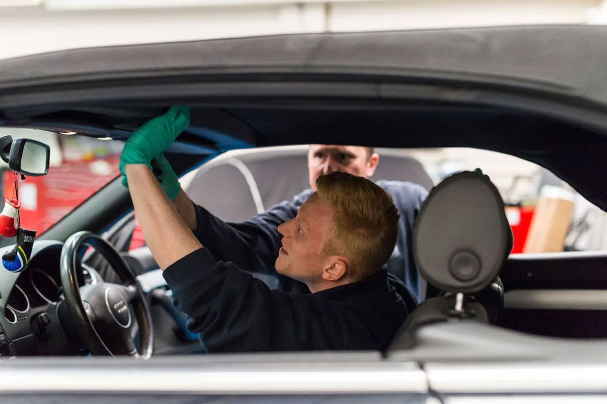 Automotive specialists cleaning and inspecting the interior seal of a convertible soft top roof to prevent leaks and wear.