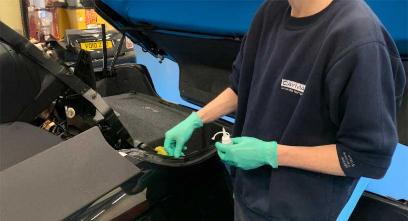 A man wearing a blue shirt and gloves is repairing a car in a garage.